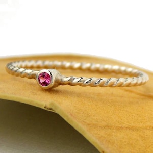 May include: A delicate silver ring with a twisted band and a small pink gemstone.