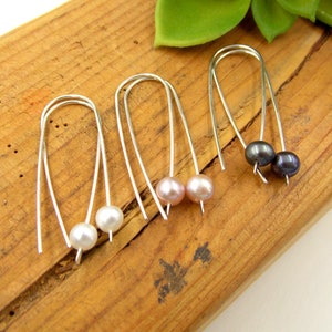 May include: Three pairs of silver hoop earrings with pearl accents. The pearls are white, pink, and black.