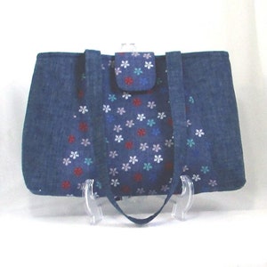 May include: A blue denim tote bag with a flap closure and two top handles. The bag is decorated with a pattern of small white, pink, red, and blue flowers.