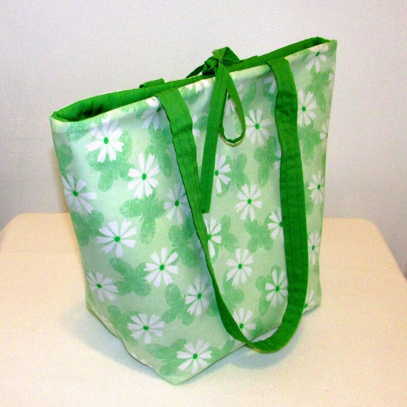May include: A green canvas tote bag with white daisy print and green straps. The bag has a green fabric lining.