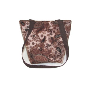 Pode incluir: Uma sacola marrom com estampa paisley e al&ccedil;as marrons escuras. A sacola apresenta um padr&atilde;o floral repetido em tons de marrom e bege. A sacola tem formato retangular e um design simples e funcional.