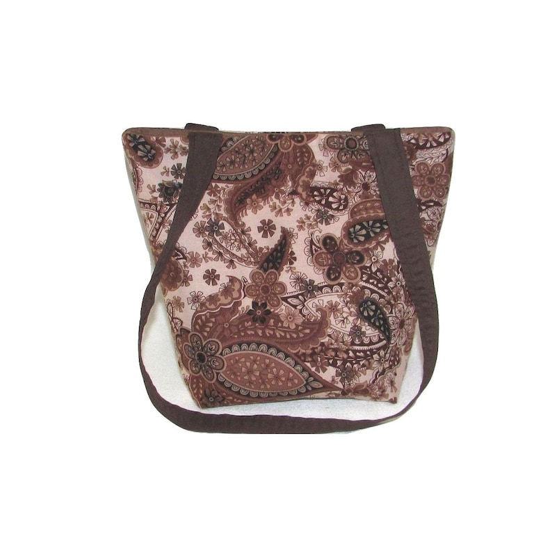 Pode incluir: Uma sacola marrom com estampa paisley e al&ccedil;as marrons escuras. A sacola apresenta um padr&atilde;o floral repetido em tons de marrom e bege. A sacola tem formato retangular e um design simples e funcional.