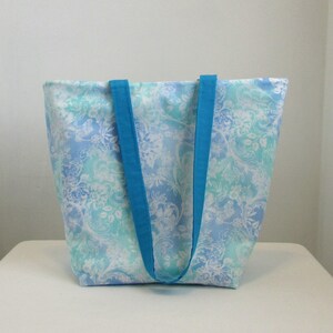 May include: A large tote bag with a blue and white floral pattern. The bag has two wide, turquoise straps.