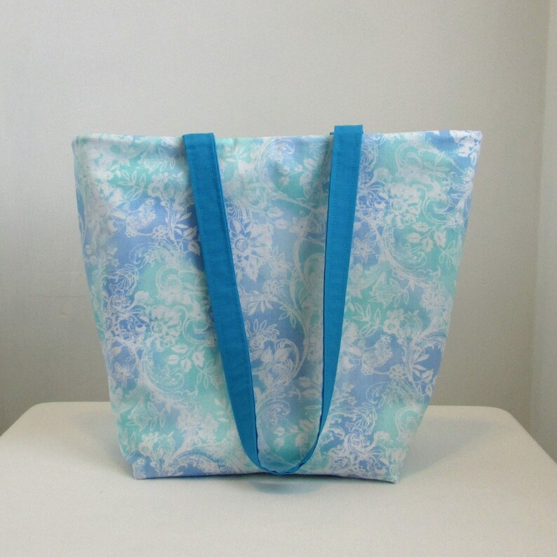 May include: A large tote bag with a blue and white floral pattern. The bag has two wide, turquoise straps.