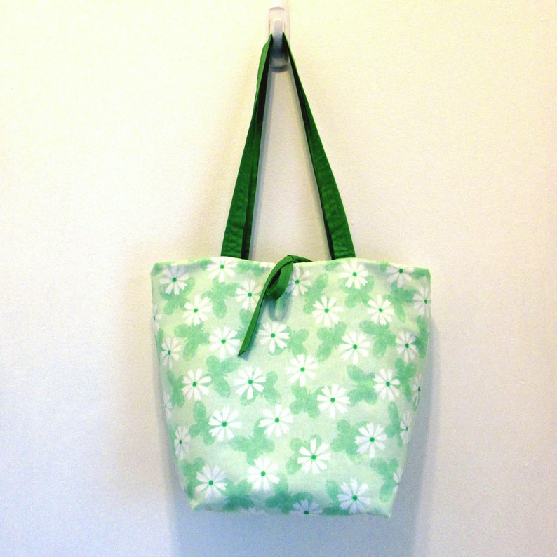 May include: A green tote bag with white daisy print. The bag has green handles.