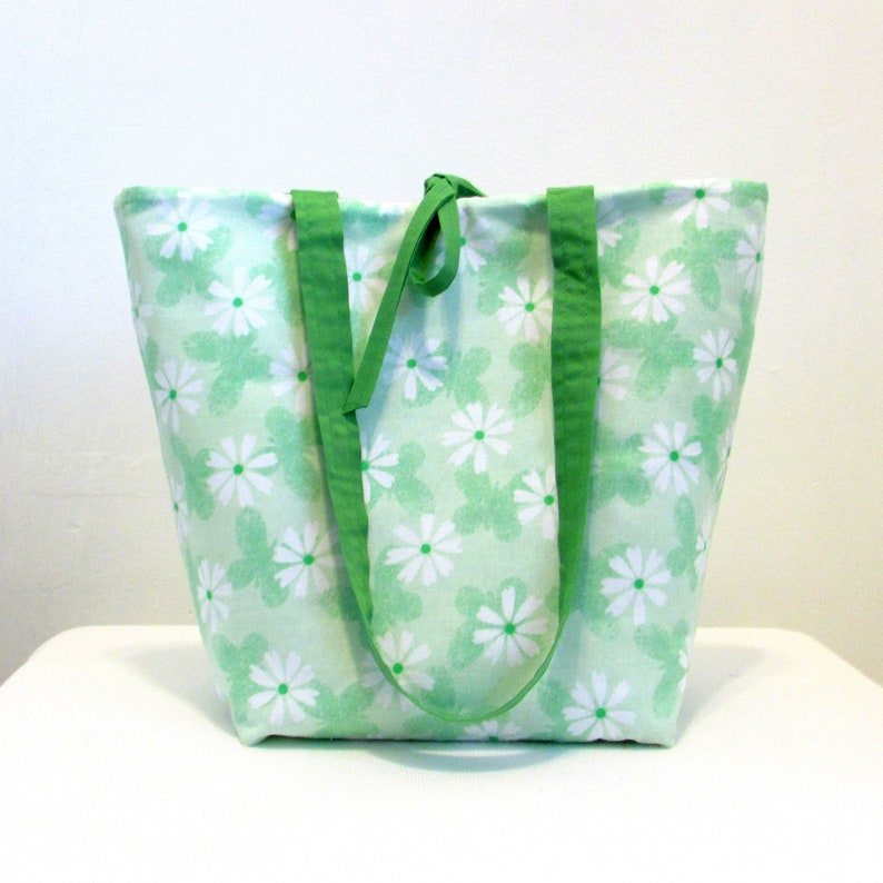 May include: A green tote bag with white daisy print and green straps.