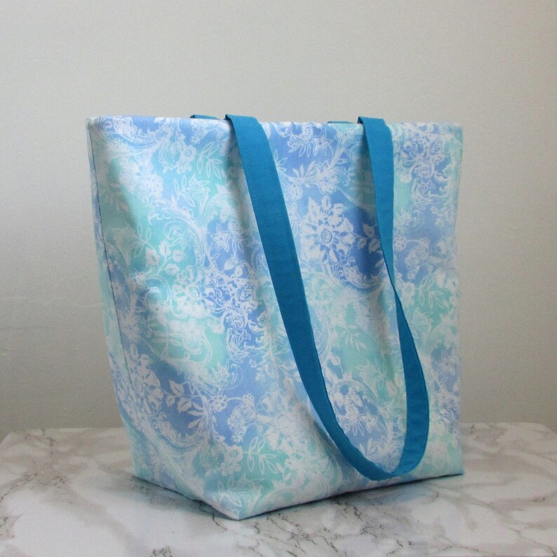 May include: A large blue and white tote bag with a floral pattern and teal blue handles.