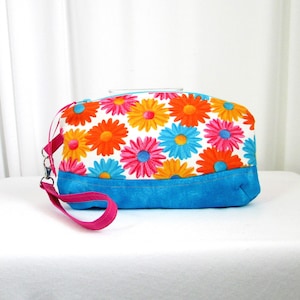 May include: A bright blue and white floral print cosmetic bag with a pink strap. The bag has a blue bottom and a white top with colorful flowers.