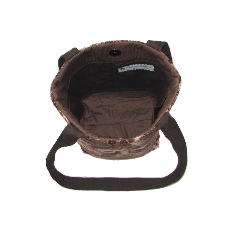 Pode incluir: Bolsa tote marrom com estampa paisley. A bolsa tem al&ccedil;as marrons escuras e fecho magn&eacute;tico. O interior &eacute; marrom liso com um pequeno bolso. A bolsa &eacute; feita de um tecido macio e acolchoado.