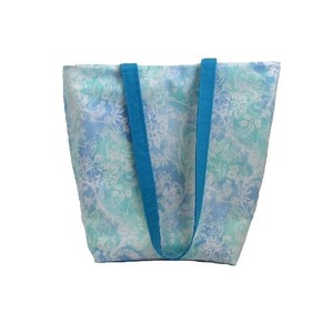 May include: A blue and white floral tote bag with turquoise straps. The bag is made of a lightweight fabric and has a spacious interior.