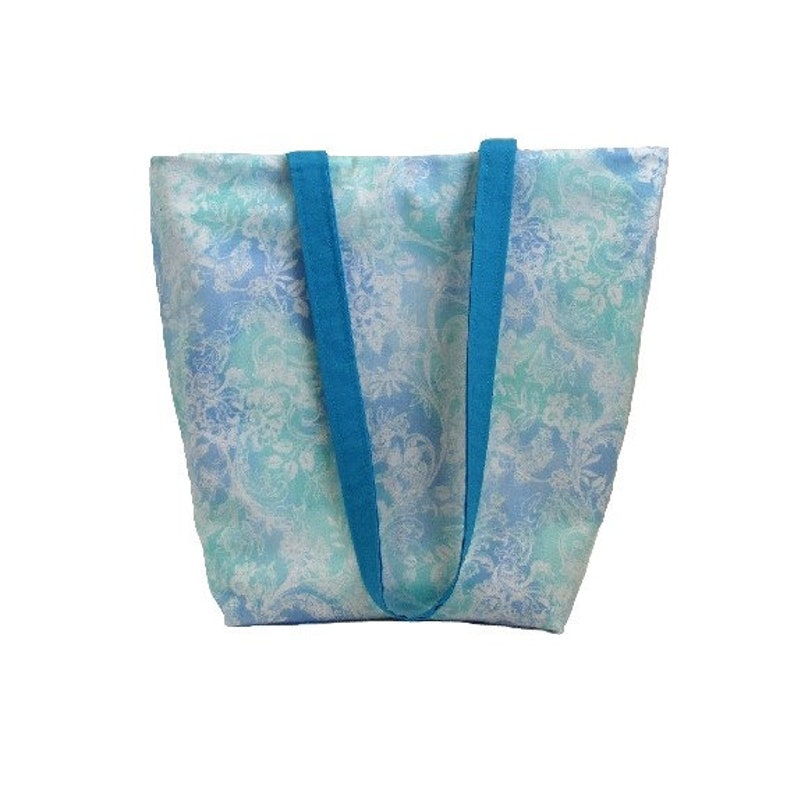 May include: A blue and white floral tote bag with turquoise straps. The bag is made of a lightweight fabric and has a spacious interior.