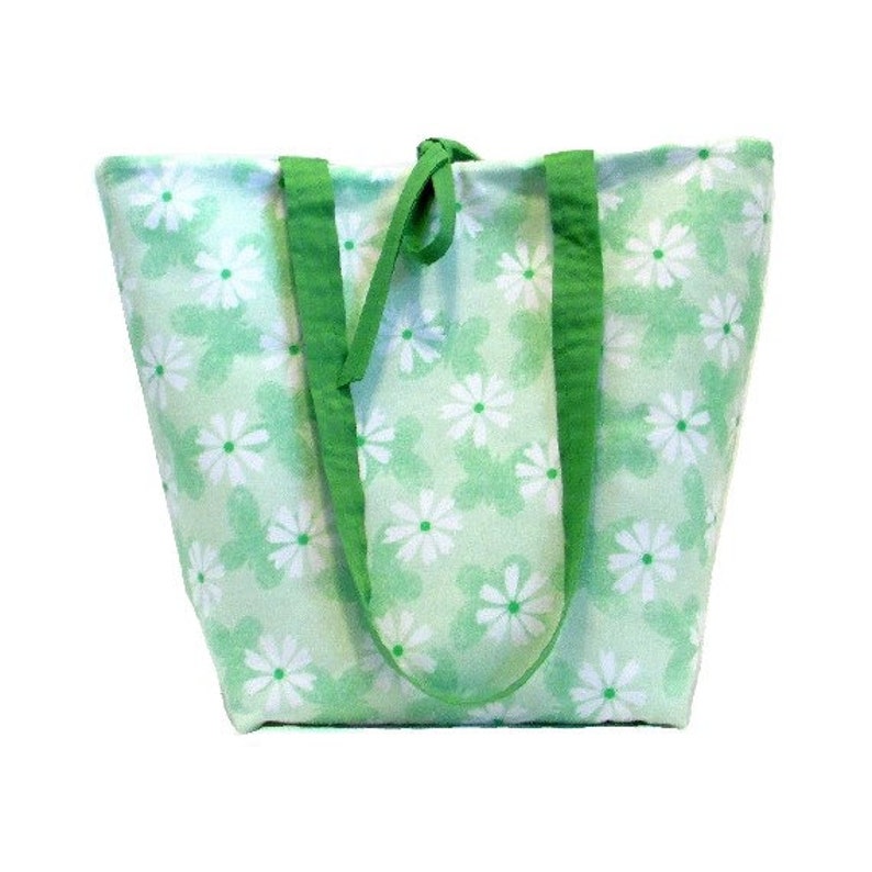 May include: A green tote bag with white floral print. The bag has two green straps and a green fabric handle.