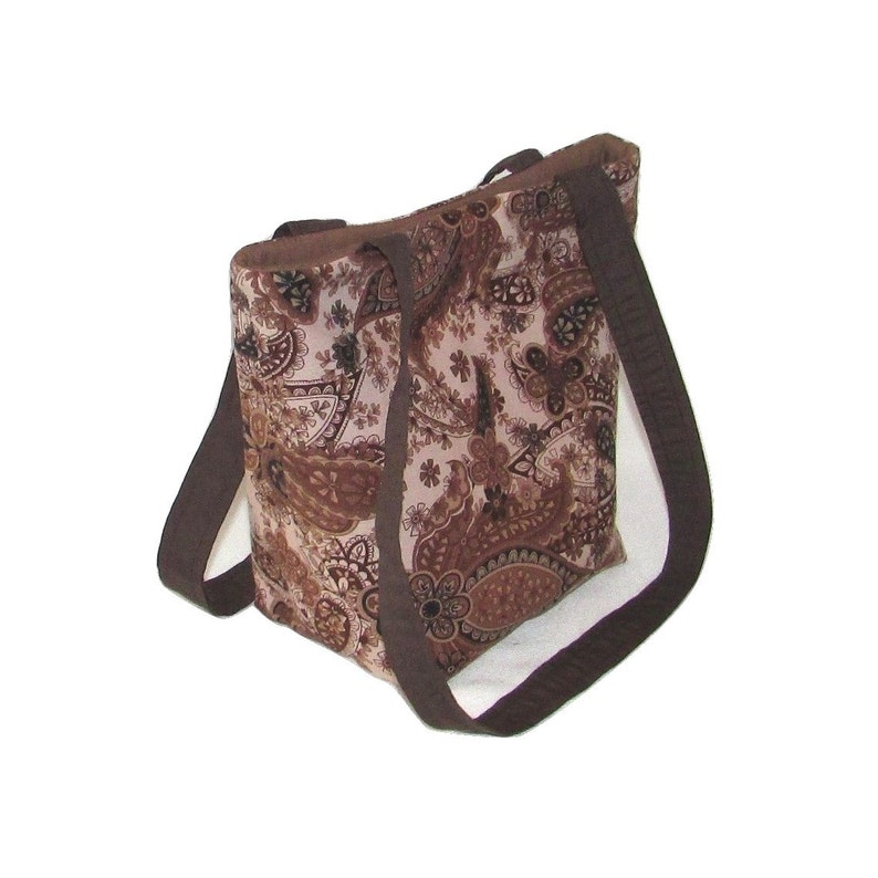 Pode incluir: Uma sacola marrom com um padr&atilde;o paisley em tons de marrom e bege. A sacola tem duas al&ccedil;as longas marrons escuras e uma borda combinando. A sacola &eacute; feita de tecido e foi projetada para transportar itens.