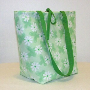 May include: A green canvas tote bag with white daisy print and green straps.