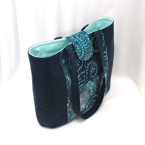 May include: A navy blue tote bag with a teal and white patterned lining. The bag has two long straps and a flap closure.