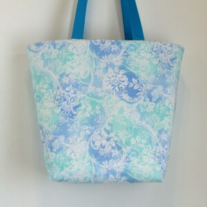May include: A blue and green tote bag with a white floral pattern. The bag has two blue handles.