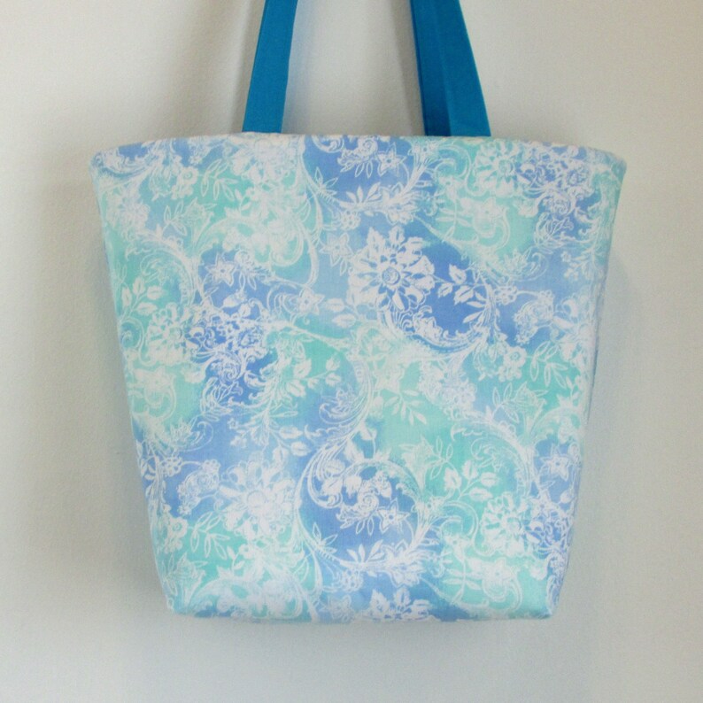 May include: A blue and green tote bag with a white floral pattern. The bag has two blue handles.