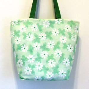 May include: A green tote bag with a white daisy print. The bag has green straps.
