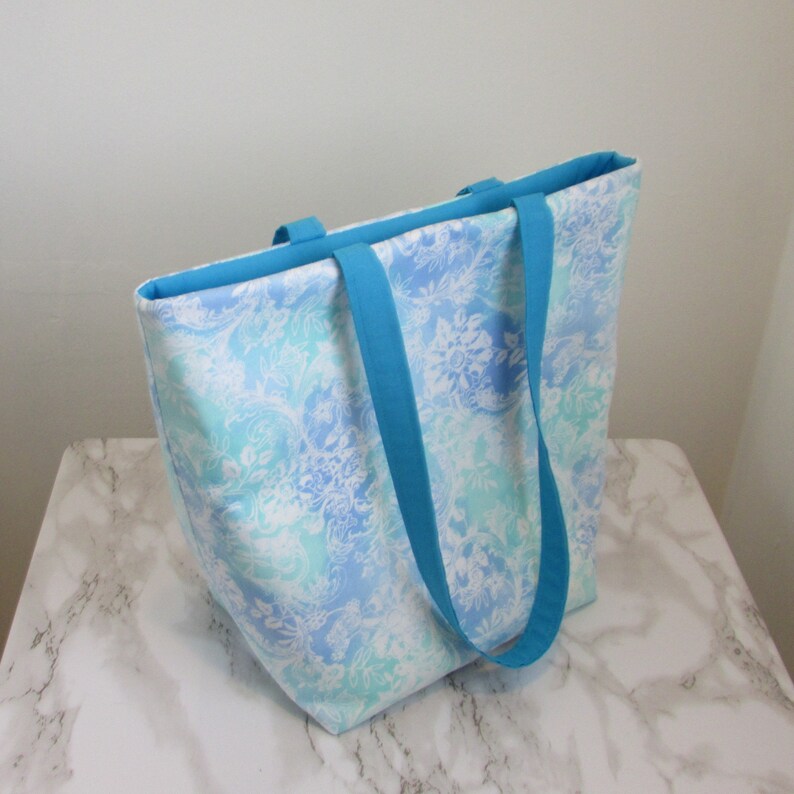 May include: A large tote bag with blue and white floral print fabric and turquoise straps.