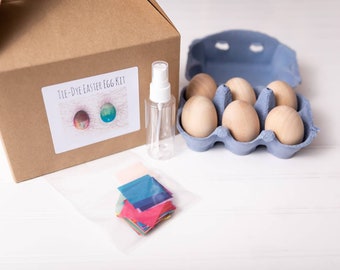 May include: A tie-dye Easter egg kit containing a brown box, six wooden eggs in a blue egg carton, a spray bottle, and a bag of colourful tissue paper.