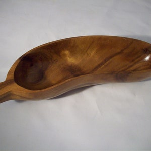 May include: A wooden serving bowl shaped like a banana, with a smooth, polished finish. The bowl is made of light brown wood with darker brown streaks.