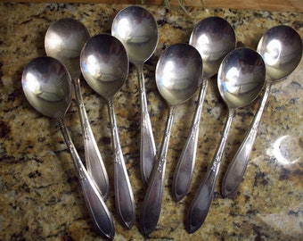 May include: Set of eight silver-plated soup spoons with ornate handles. The spoons are arranged in a fan shape on a granite countertop.