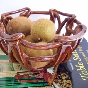 May include: A brown ceramic fruit bowl with a unique, twisted design. The bowl is filled with kiwi fruit.