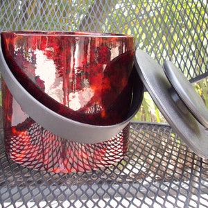 May include: A red and black ice bucket with a black lid and handle. The bucket is made of glass and has a textured surface.