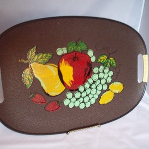May include: A brown oval serving tray with a painted design of fruit. The tray has two beige handles on the sides. The fruit design includes a red apple, a yellow pear, green grapes, and red strawberries.