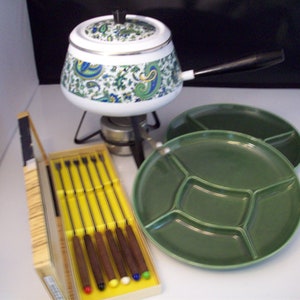 Puede incluir: Un juego de fondue vintage con una olla de patrón blanco y verde, un plato de cerámica verde con cuatro secciones y una caja de madera que contiene seis tenedores de fondue.