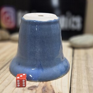 May include: A blue ceramic planter with a flared base and a white interior rim. A red die with white dots sits next to the planter on a wooden surface. The planter has a glossy finish.