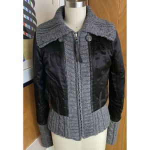 May include: A black and grey cropped jacket with a knitted collar and zip fastening. The jacket has a satin-like finish and a knitted bottom.