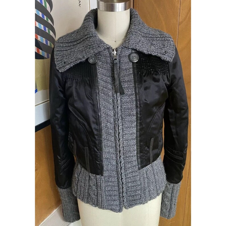 May include: A black and grey cropped jacket with a knitted collar and zip fastening. The jacket has a satin-like finish and a knitted bottom.
