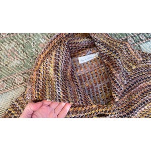 K&ouml;nnte beinhalten: Eine mehrfarbige Strickjacke in Braun-, Gelb- und Oranget&ouml;nen. Das Etikett lautet "Charles & Robin". Die Strickjacke hat einen Schalkragen und einen Knopfverschluss. Das Strickmuster ist strukturiert und scheint eine Mischung aus Wolle und anderen Fasern zu sein.