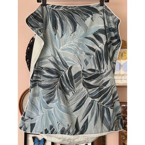 May include: A light gray and blue botanical print fabric with a white border. The fabric features a repeating pattern of large leaves in shades of gray and blue. The fabric is likely used for home decor or apparel.