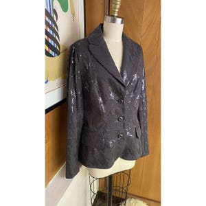 K&ouml;nnte beinhalten: Ein schwarzer Blazer mit silbernen Pailletten. Der Blazer hat einen Schalkragen, einen einreihigen Verschluss und zwei Eingrifftaschen.