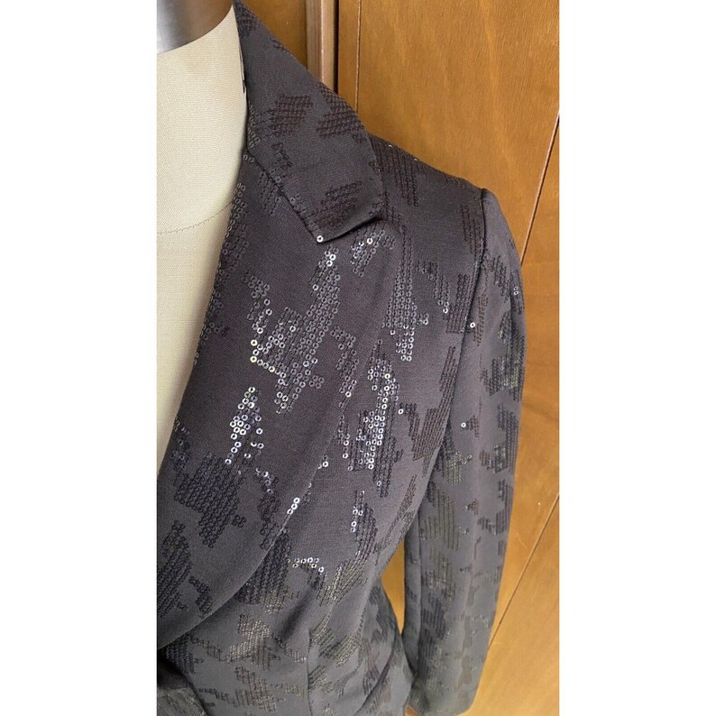 K&ouml;nnte beinhalten: Ein schwarzer Blazer mit einem Paillettenmuster. Die Pailletten sind in einem geometrischen Muster angeordnet.