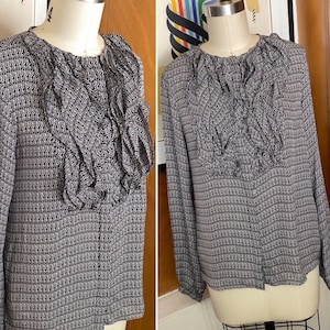 以下が含まれることがあります： 黒と白のパターンでデザインされたブラウス。大きなフリル襟と長袖、体にフィットするシルエットです。