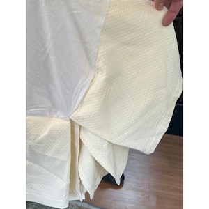 May include: Cream-colored bed skirt with a diamond pattern and a smooth, white top section. The skirt is folded, revealing the textured fabric and the underside. The overall look is clean and classic.