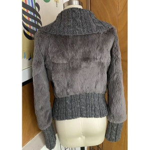 May include: A grey faux fur jacket with a cable knit collar and cuffs. The jacket has a cropped length and a fitted silhouette.