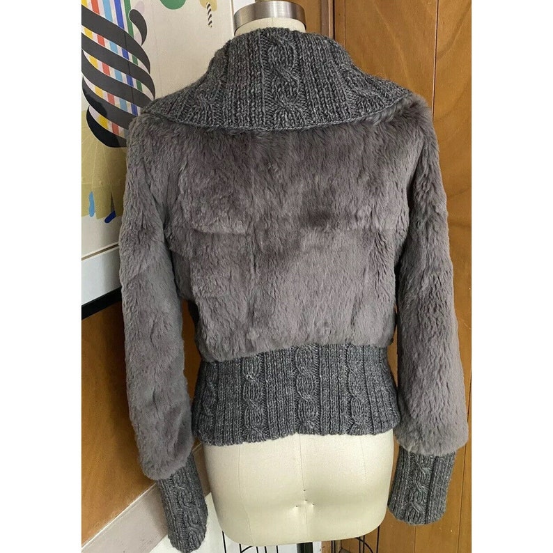May include: A grey faux fur jacket with a cable knit collar and cuffs. The jacket has a cropped length and a fitted silhouette.