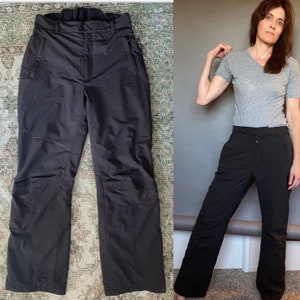 May include: Black ski trousers with a zipped pocket on each leg. The trousers have a straight leg and a high waist.