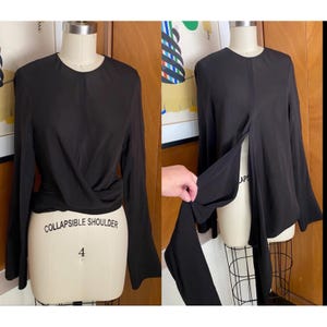 May include: Black long-sleeve top with a wrap-style front and flared sleeves. The top is displayed on a mannequin with the text "COLLAPSIBLE SHOULDER" and the number "4". The top has a round neckline and a split front design.