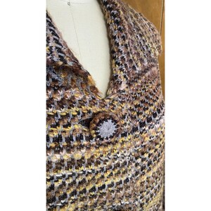 K&ouml;nnte beinhalten: Nahaufnahme eines mehrfarbigen Strickkleidungsst&uuml;cks mit Knopfverschluss. Die Farben sind Braun, Gelb, Grau und Schwarz. Der Knopf ist ein rundes, grau-braunes Design. Das Kleidungsst&uuml;ck wird auf einer Schaufensterpuppe pr&auml;sentiert.