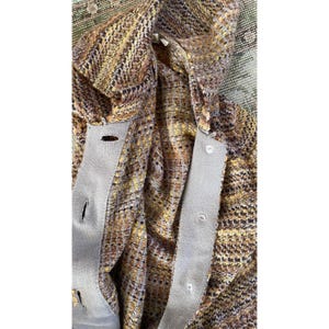 K&ouml;nnte beinhalten: Nahaufnahme einer mehrfarbigen Tweed-Strickjacke mit Knopfleiste. Der Stoff weist eine Mischung aus braunen, gelben und schwarzen F&auml;den auf. Die Strickjacke hat einen hellgrauen Besatz entlang der Knopfleiste und um die Knopfl&ouml;cher.