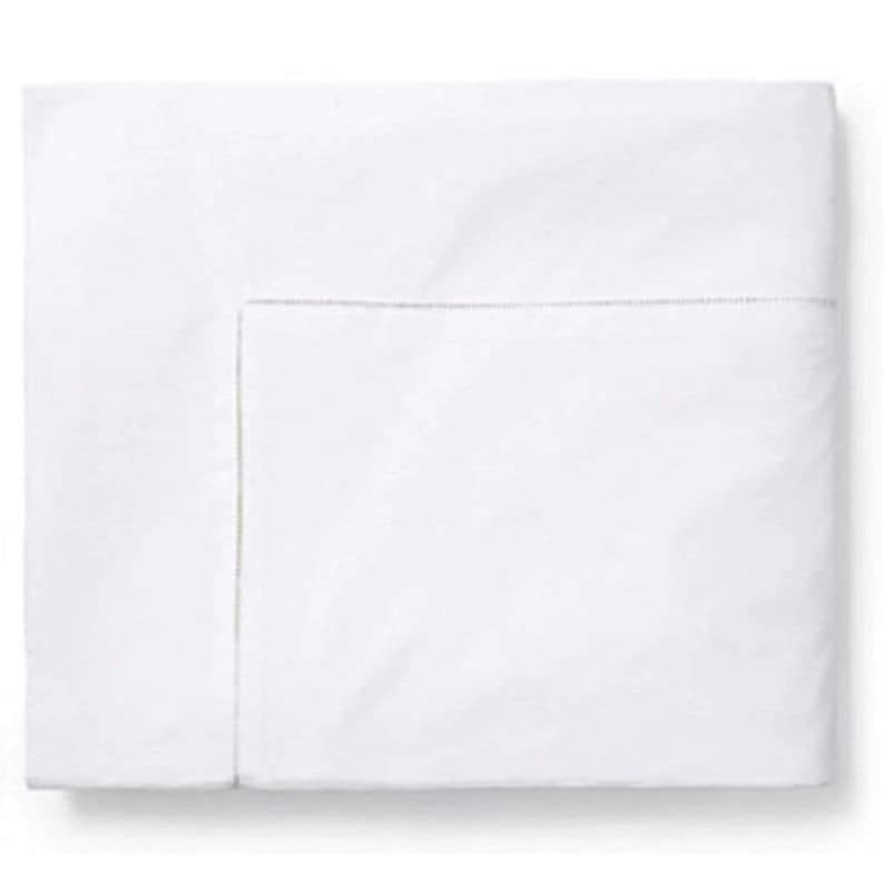 Pu&ograve; includere: Un lenzuolo bianco piegato con un bordo cucito sottile. Il lenzuolo &egrave; pulito e fresco, suggerendo un prodotto di lino di alta qualit&agrave;. Il design semplice e il colore bianco brillante danno un senso di purezza e comfort, adatto per una camera da letto.