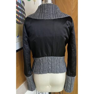 May include: A black satin jacket with a grey cable knit collar and cuffs. The jacket is cropped and has a fitted silhouette.