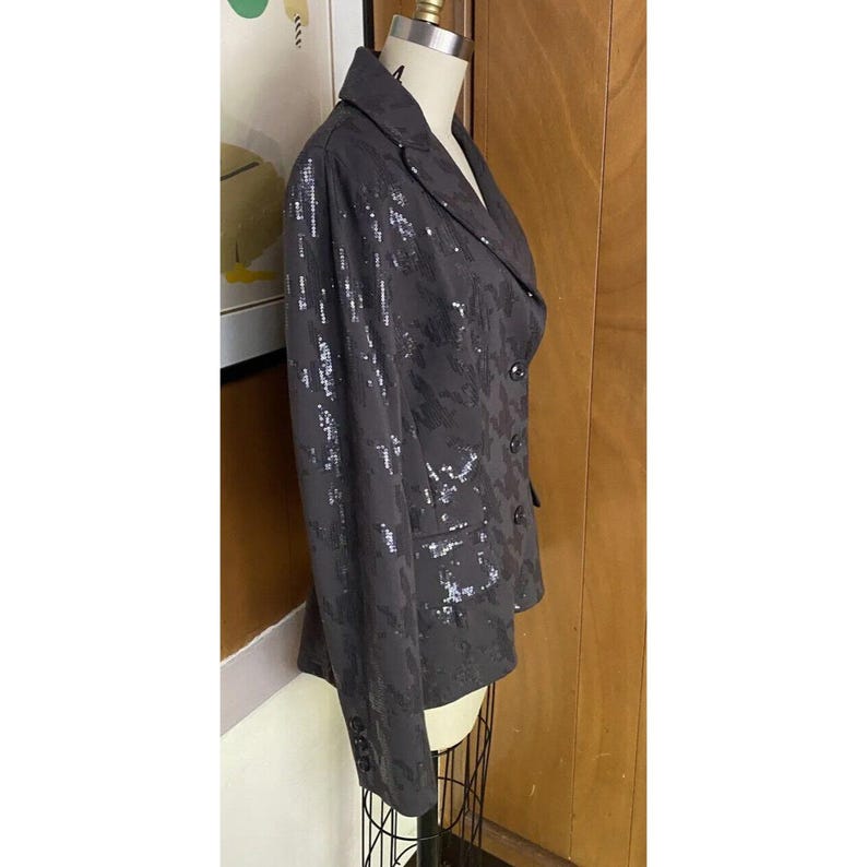 K&ouml;nnte beinhalten: Ein schwarzer Blazer mit einem silbernen Paillettenmuster. Der Blazer hat einen Schalkragen, lange &Auml;rmel und einen zweireihigen Verschluss.