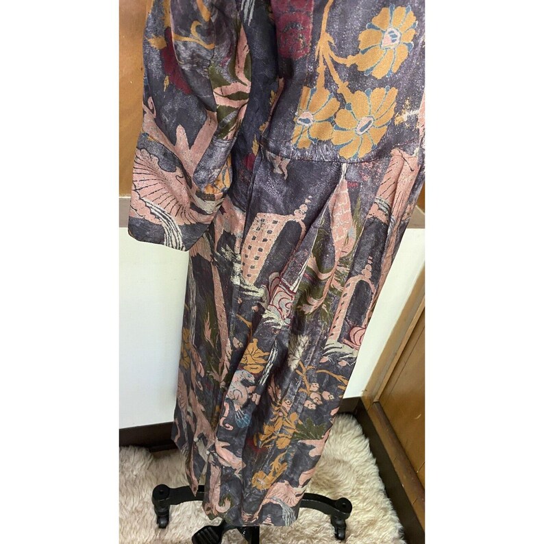 Op de afbeelding: Een lange, vloeiende jurk met een donkere achtergrond en een kleurrijke bloemenprint. De jurk heeft een geplooide rok en lange mouwen.