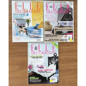 Puede incluir: Tres ejemplares de la revista Elle Decoration, una revista de decoración del hogar. Las portadas presentan imágenes coloridas de diseño de interiores y decoración del hogar. La primera portada presenta un sillón azul y un arreglo floral. La segunda portada presenta un dormitorio con una cama con dosel y una lámpara colgante. La tercera portada presenta una cama blanca con una pantalla negra y un arreglo floral.